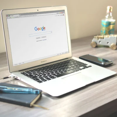 A neat workspace featuring a laptop displaying Google search, a smartphone, and a notebook on a wooden desk.